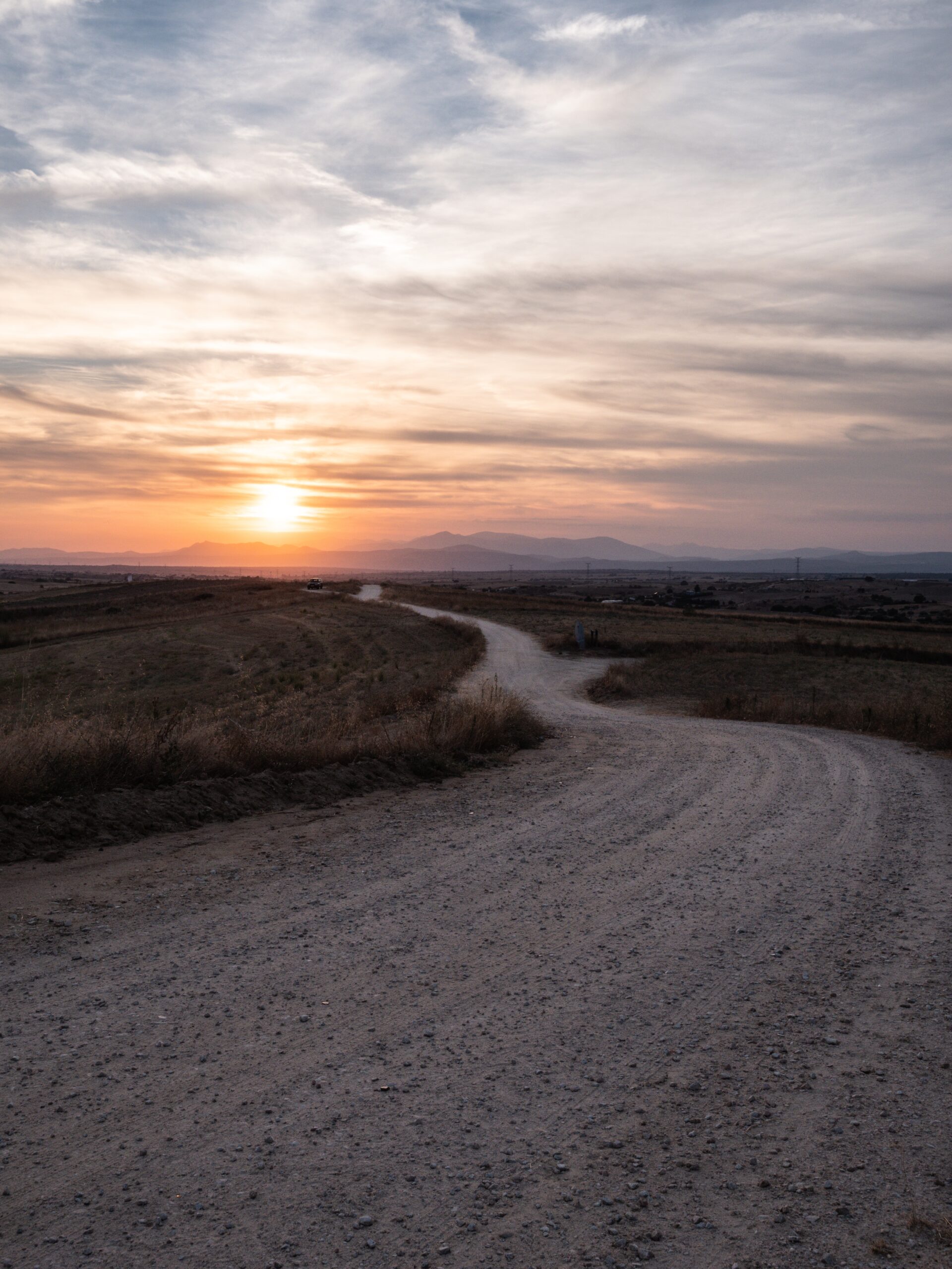 A vertical shot of a pathway in a grassy field with the breathtaking view of sunset in the background